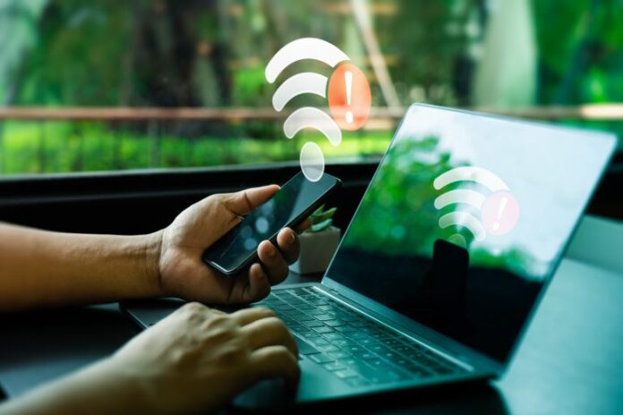 Um homem mexe no celular e no laptop e um sinal de wi-fi com uma exclamação está em cima da foto